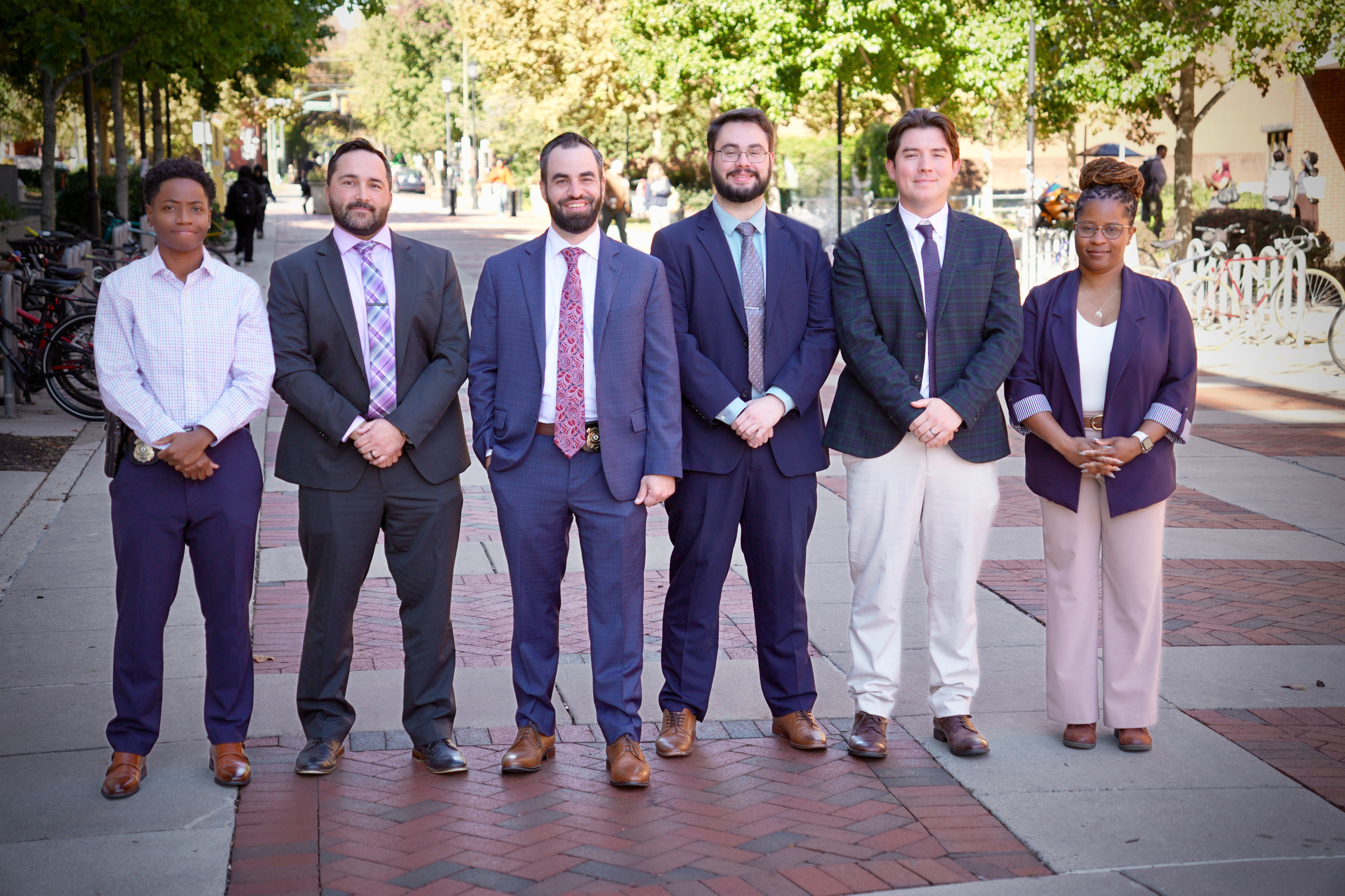 A group of six police detectives smiling for a team photo outside on VCU's campus
