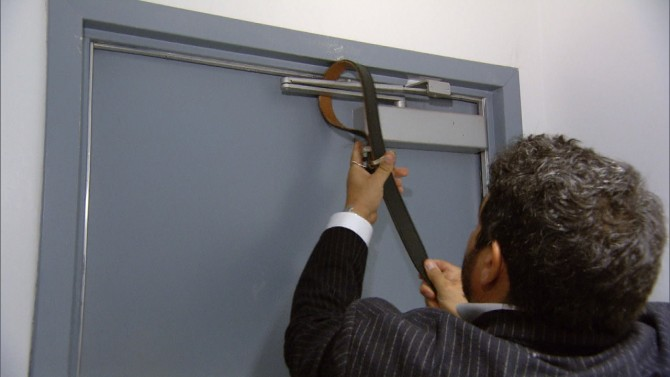 Photo: a person uses a belt to secure the arm at the top of a door. 