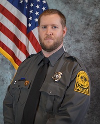 Picture of Officer Luke Shrader in VCU PD uniform, from approximately waist up, sitting in front of an American flag.