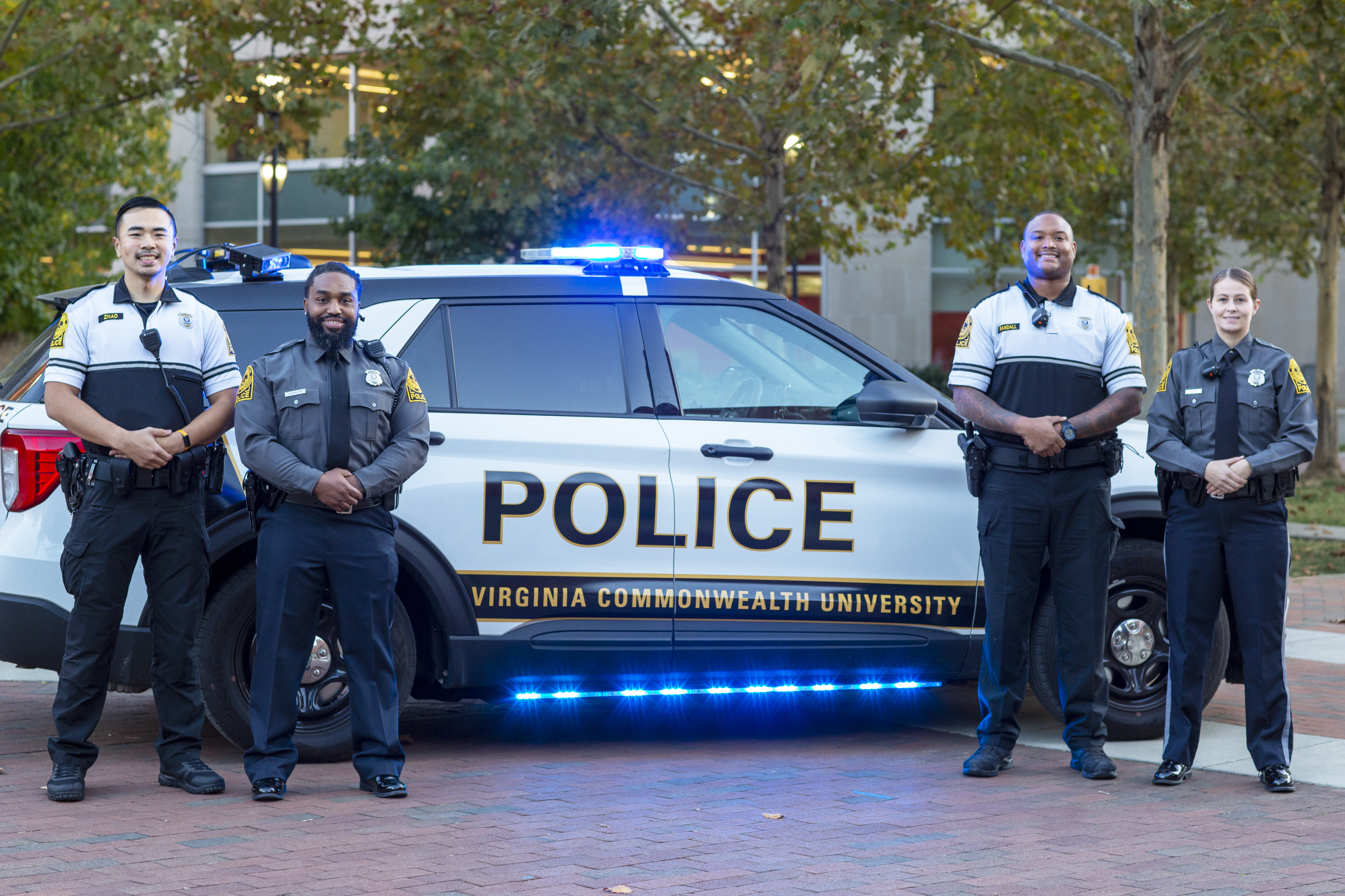 Four V-C-U Police officers stand in front of a patrol vehicle on the university's Monroe Park Campus.